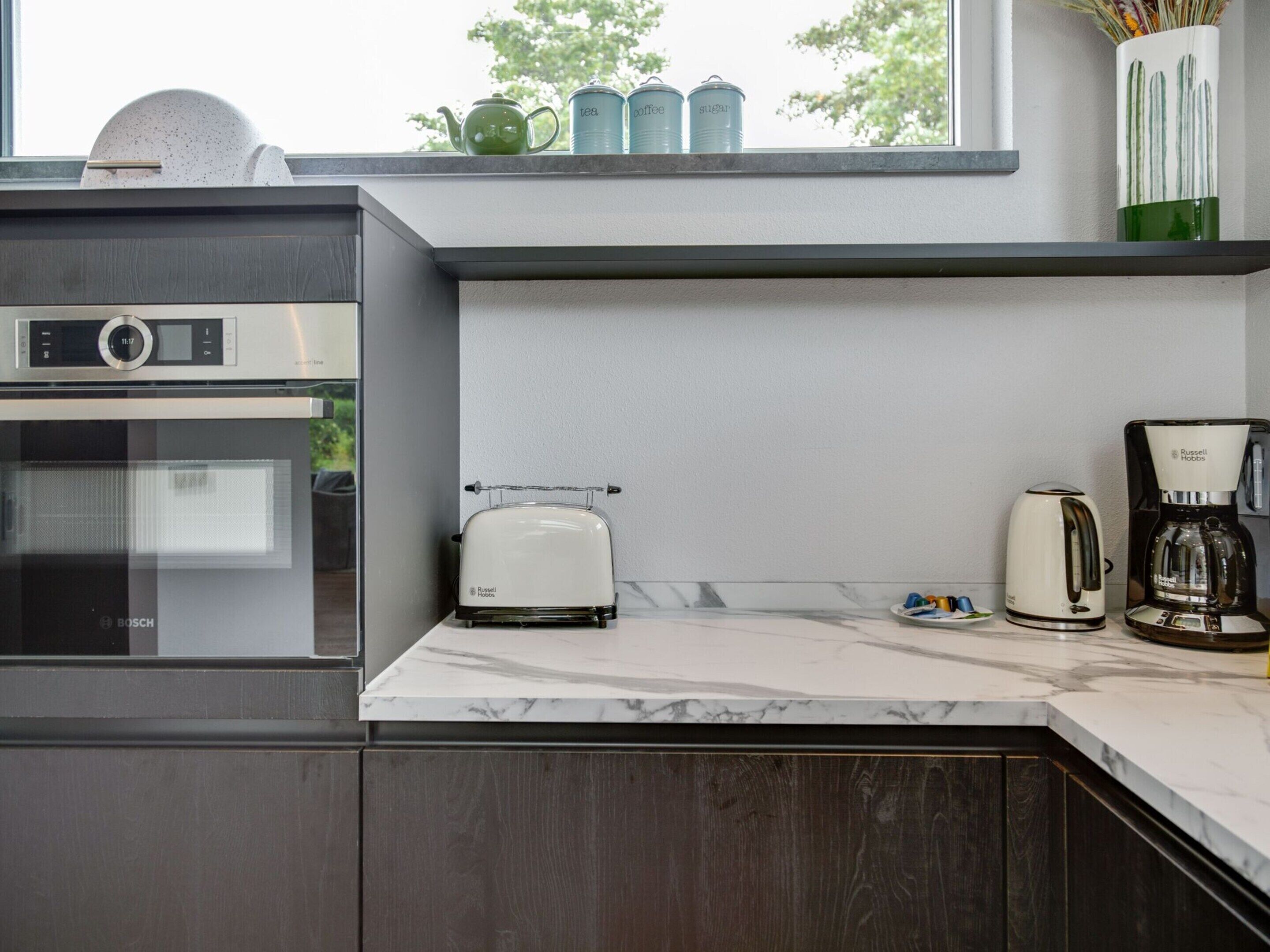 Une cuisine moderne équipée d’un four Bosch, d’un grille-pain blanc, d’une machine à café et d’une bouilloire posés sur le plan de travail.