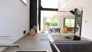 Eine moderne Küche mit einer großen Kochinsel, einem Essbereich mit Tisch und Stühlen sowie Blick ins Freie.