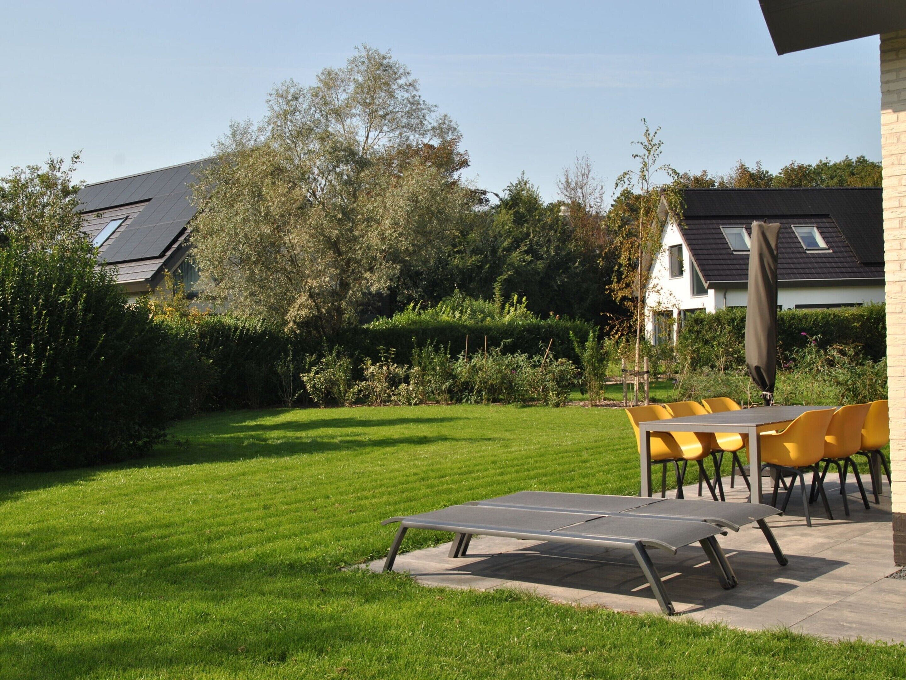 A well-maintained lawn with a dining area featuring yellow chairs and a table.