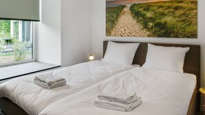Ein Schlafzimmer mit einem großen Bett, einem Fenster mit Blick ins Freie und einem Gemälde einer Strandlandschaft an der Wand.