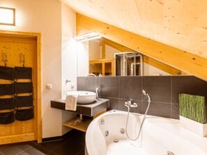 A bathroom with a bathtub, a sink, and a mirror. There is a wooden door and a towel rack. - Spacious Chalet With hot tub (Sankt Georgen am Kreischberg)