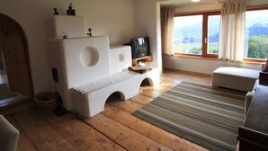 A room with a wooden floor, a television on a stand, a window with curtains, and a view of the outdoors. - Holiday Home in Liebenfels in Carinthia With Sauna (Liebenfels)