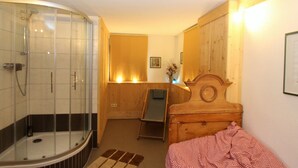 A room with a glass-enclosed shower, a wooden bed, a small table, and a chair. - Holiday Home in Liebenfels in Carinthia With Sauna (Liebenfels)