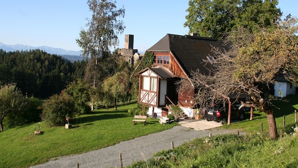 A traditional wooden house with a sloped roof, a stone tower, and a well-maintained garden with a gravel path. - Holiday Home in Liebenfels in Carinthia With Sauna (Liebenfels)