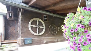 A wooden building with a large wheel and a hanging flower basket. - Holiday Home in Liebenfels in Carinthia With Sauna (Liebenfels)