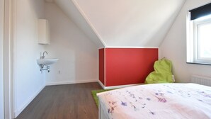 Una camera da letto con soffitto spiovente, un lavandino bianco montato a parete, una parete d’accento rossa, un cuscino verde e una coperta con motivo floreale.