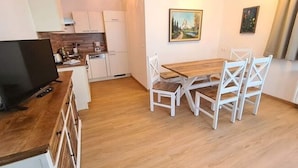 A compact kitchen with white cabinets, a wooden dining table with white chairs, and a painting on the wall. - Cozy Apartment near Ski Area in Bad Kleinkirchheim (Bad Kleinkirchheim)