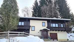 A two-story building with a symmetrical facade, a central entrance with a dark wooden door, and a small porch with a railing. - Cozy Apartment near Ski Area in Bad Kleinkirchheim (Bad Kleinkirchheim)