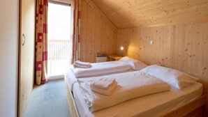 Ein Holzhütten-Zimmer mit zwei Betten, einem kleinen Tisch und einem Fenster mit Vorhängen.