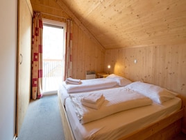 Una habitación de cabaña de madera con dos camas, una mesita y un ventanal con cortinas.