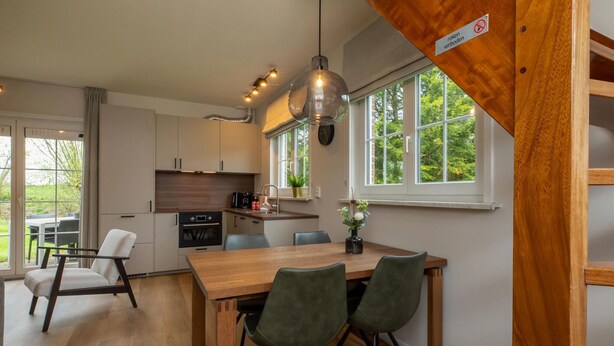 A modern kitchen with a wooden dining table, chairs, and pendant lighting.