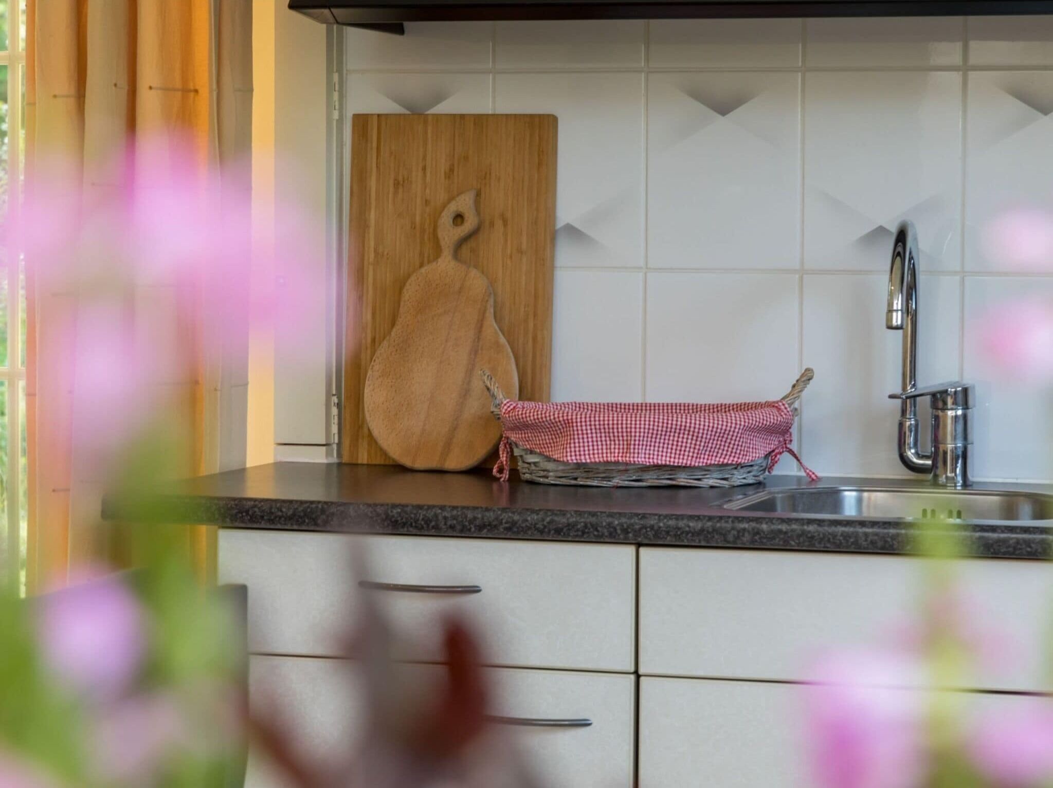 A kitchen with a wooden cutting board, a checkered cloth, and a stainless steel sink.