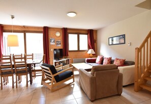 A living room with a wooden dining table, chairs, a sofa, a TV, and a lamp. - Apartment in La Chapelle Near Ski Lift (La Chapelle-d'Abondance)