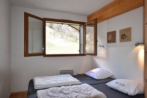 A bedroom with two beds, a window with a view of a grassy area, and two wall-mounted artworks. - Apartment in La Chapelle Near Ski Lift (La Chapelle-d'Abondance)