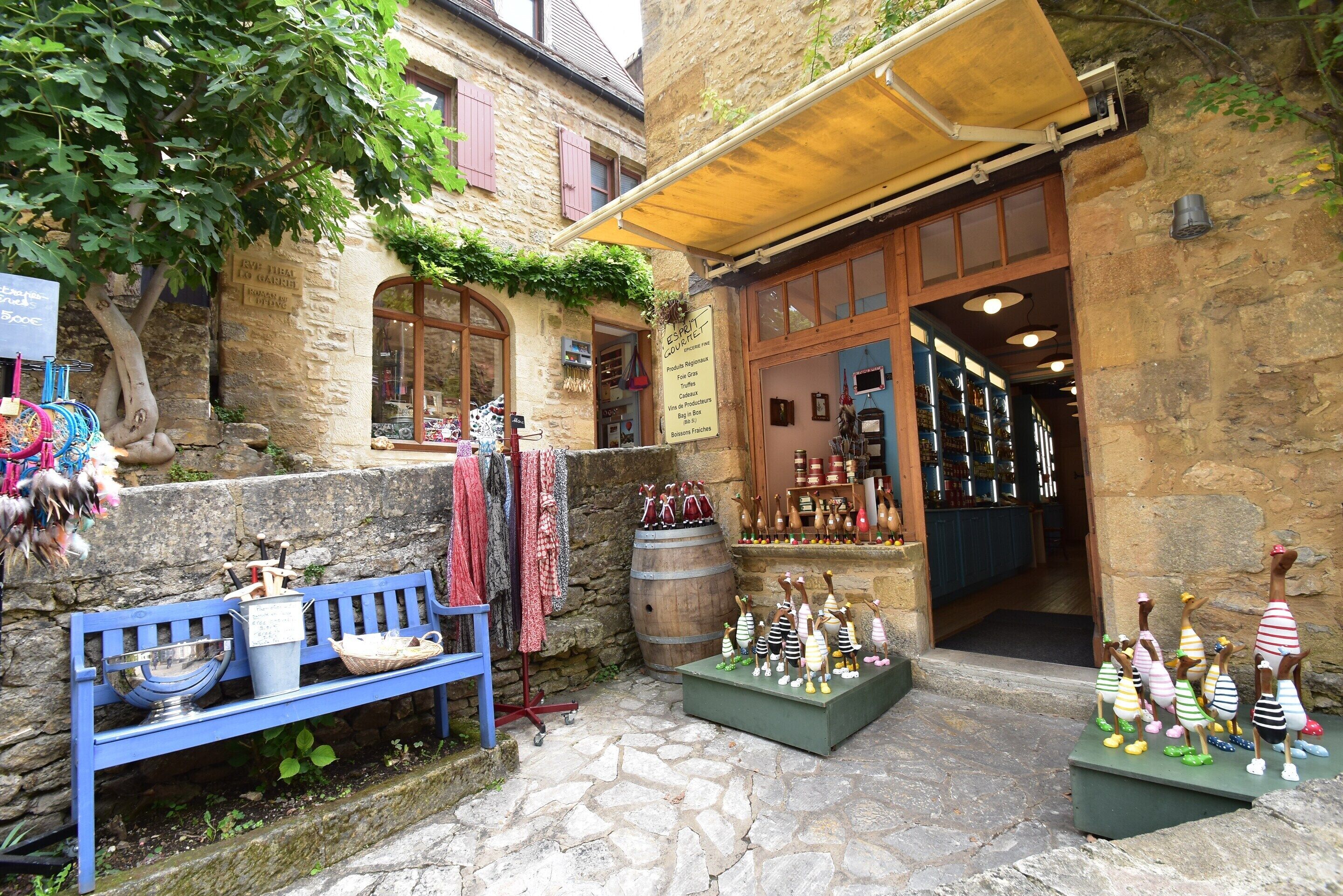 Un bâtiment en pierre avec une porte en bois, un banc et divers objets exposés à l’extérieur.