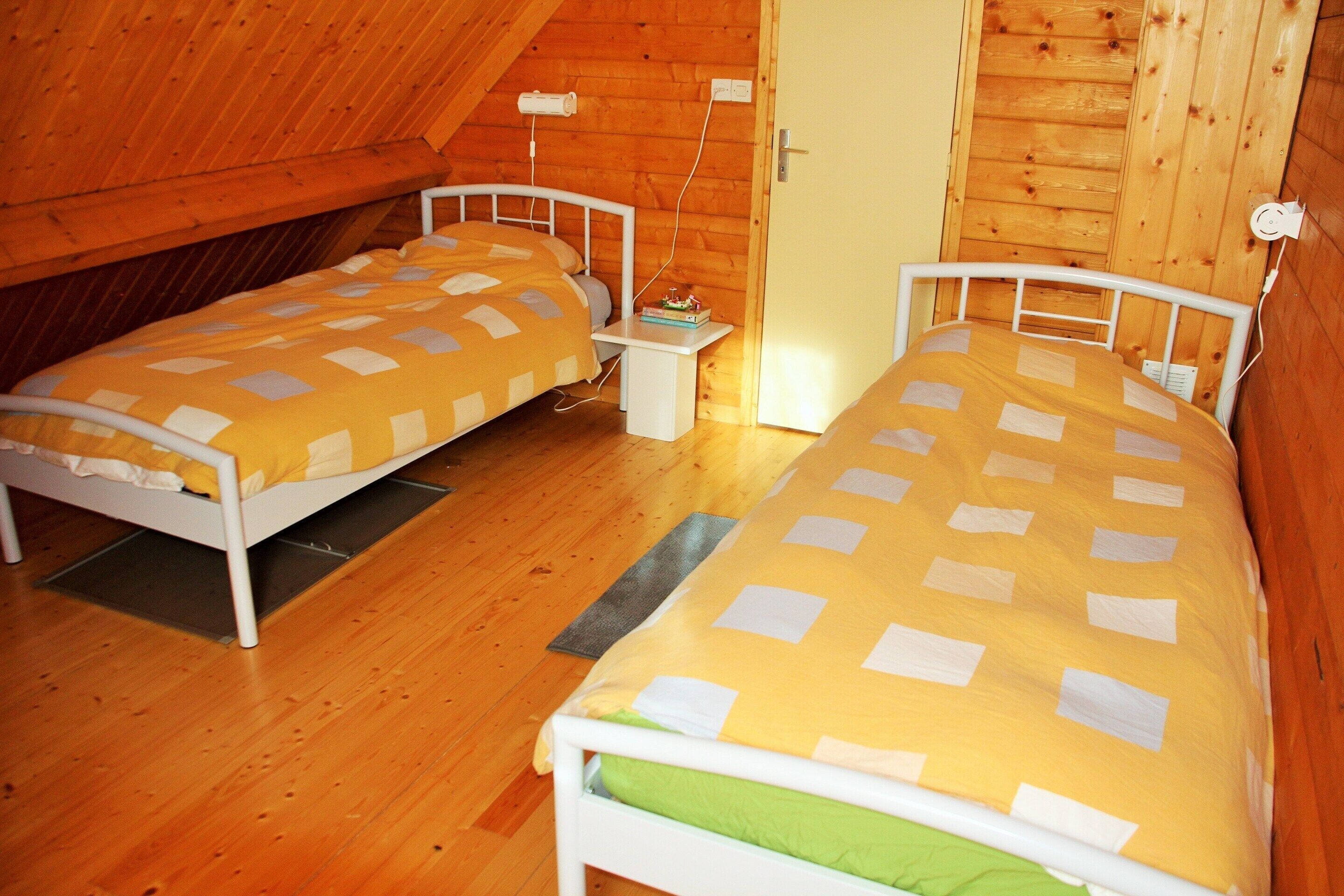 Una habitación con dos camas, paredes de madera, una puerta y una mesita de noche pequeña.
