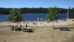 A beach with picnic tables, a flagpole, and a view of the water. - Lakeside Escape for 6 Guests (Beaulieu)