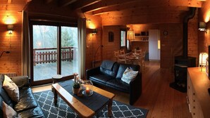A cozy cabin interior with a wooden floor, a black leather sofa, a dining table, and a fireplace. - Lakeside Escape for 6 Guests (Beaulieu)