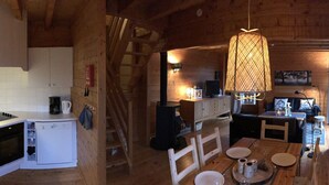 A compact cabin with a kitchenette, dining area, and a large window overlooking a forest. - Lakeside Escape for 6 Guests (Beaulieu)