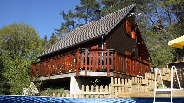 A wooden cabin with a balcony, a swimming pool, and a wooden fence. - Lakeside Escape for 6 Guests (Beaulieu)
