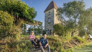 Un bâtiment en pierre doté d’un toit à deux versants, entouré de verdure et surplombé d’un ciel dégagé.