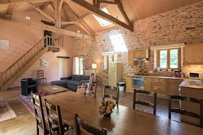A rustic interior with a wooden dining table, stone walls, a staircase, and a kitchen area. - Cottage in Chaleix Near Forest & Lake (Chalais)