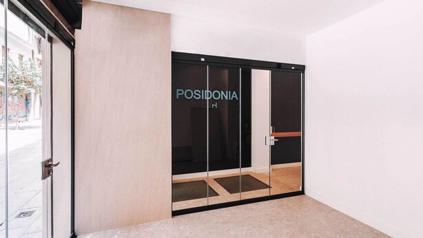 Entrada moderna de un hotel con puerta de cristal que dice "POSIDONIA".