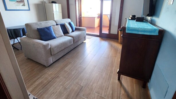 Una sala de estar con un sofá, un aparador de madera, un televisor y un ventanal corredizo que da a un espacio exterior.