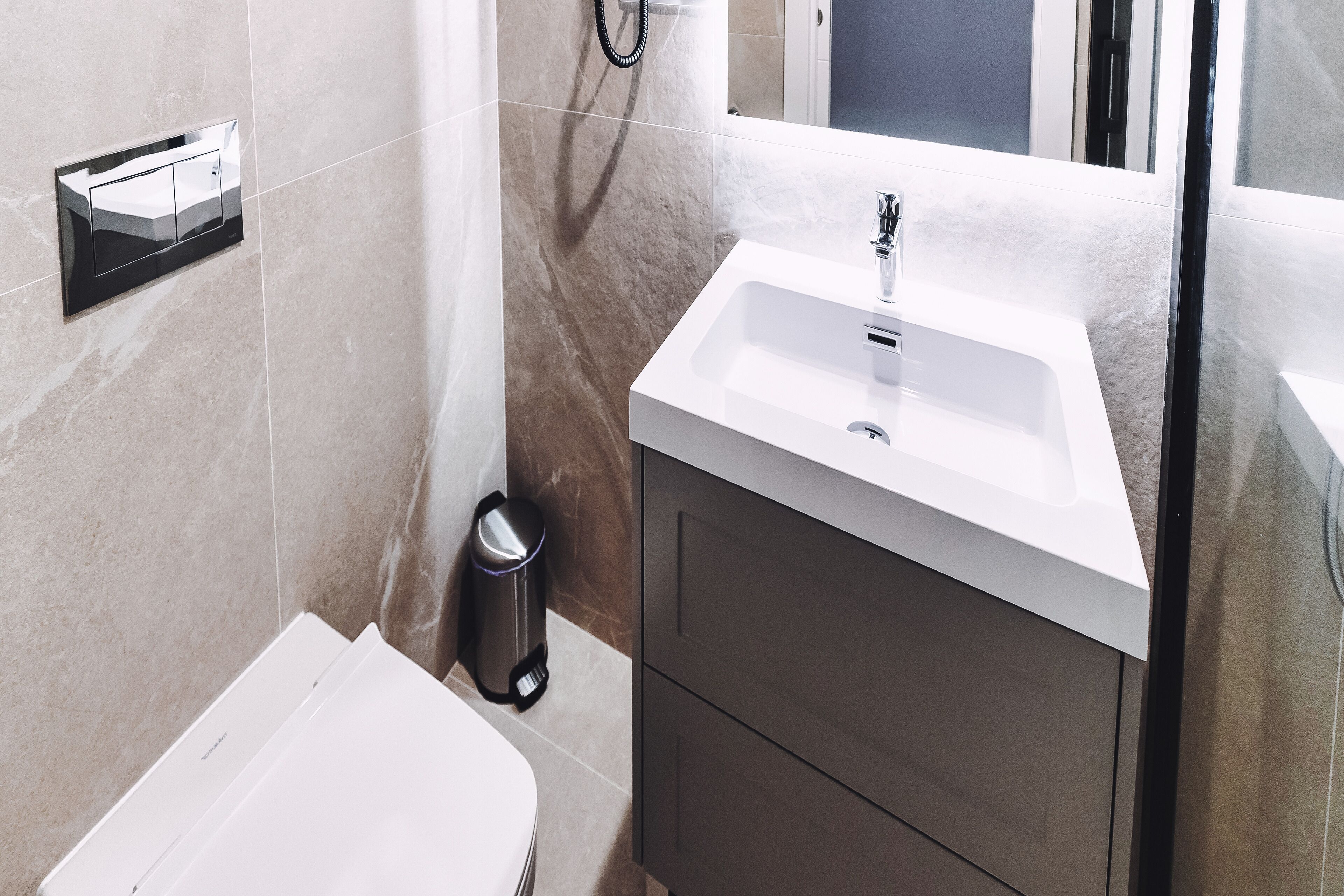 A modern bathroom with a white sink, dark cabinets, and a trash can.