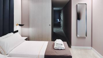 A hotel room with a bed, a bedside table, a folded towel, a mirror, and a door leading to a hallway.