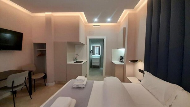 Habitación de hotel con cama, escritorio, silla, televisor, lavamanos y espejo.