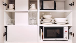 Una cocina con armarios blancos, un microondas y diferentes platos y vasos.