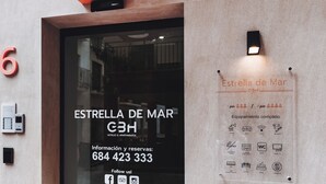 Entrada de hotel con puerta de vidrio que muestra el nombre 'Estrella de Mar' y servicios como Wi-Fi, TV y una caja fuerte.