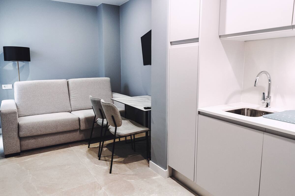 Una kitchenette compacta con un lavamanos, un pequeño comedor con una mesa y sillas, y un sofá.