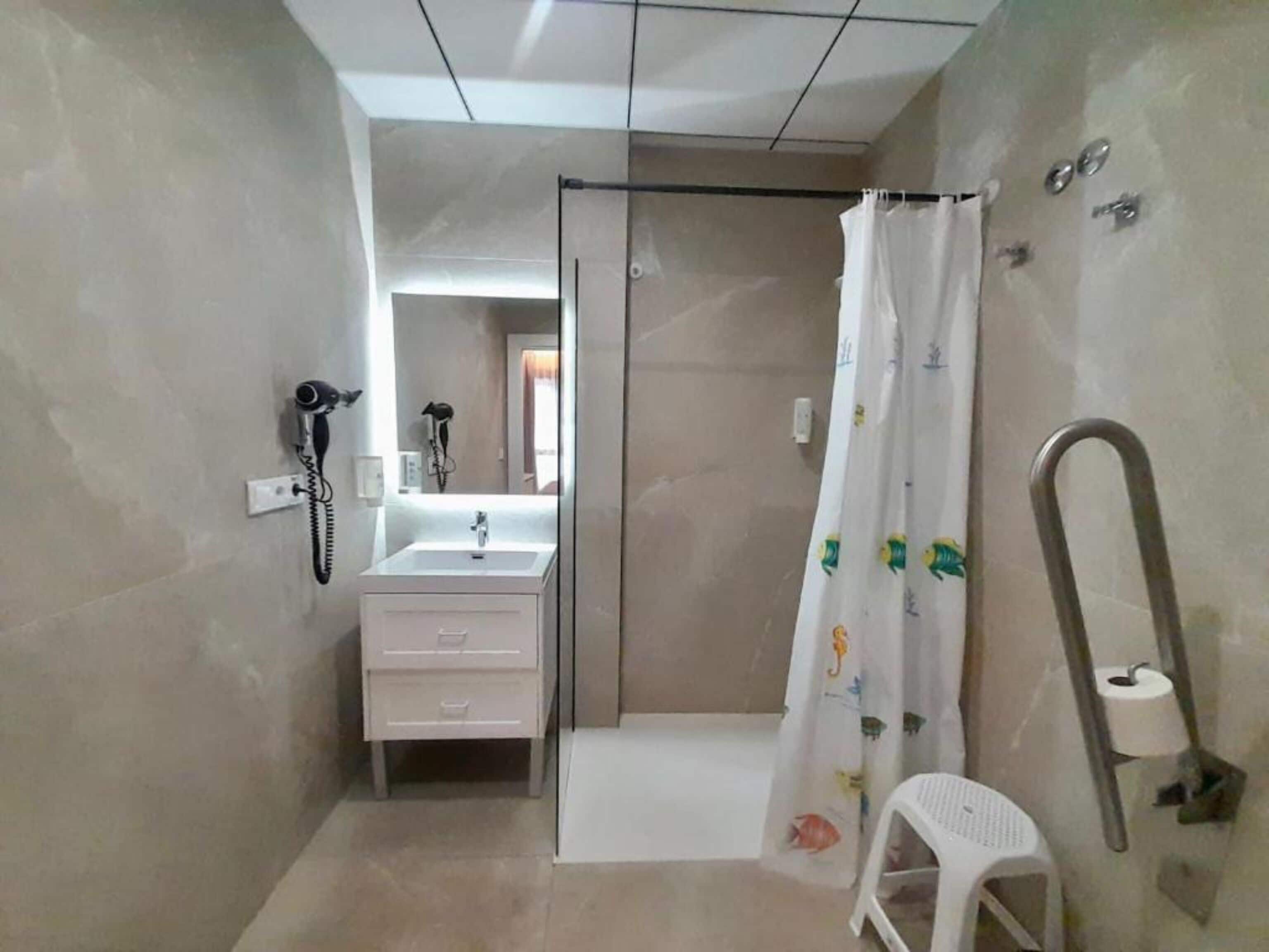 A bathroom with a shower, a sink, a toilet, and a small white stool.
