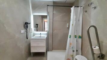 A bathroom with a shower, a sink, a toilet, and a small white stool.