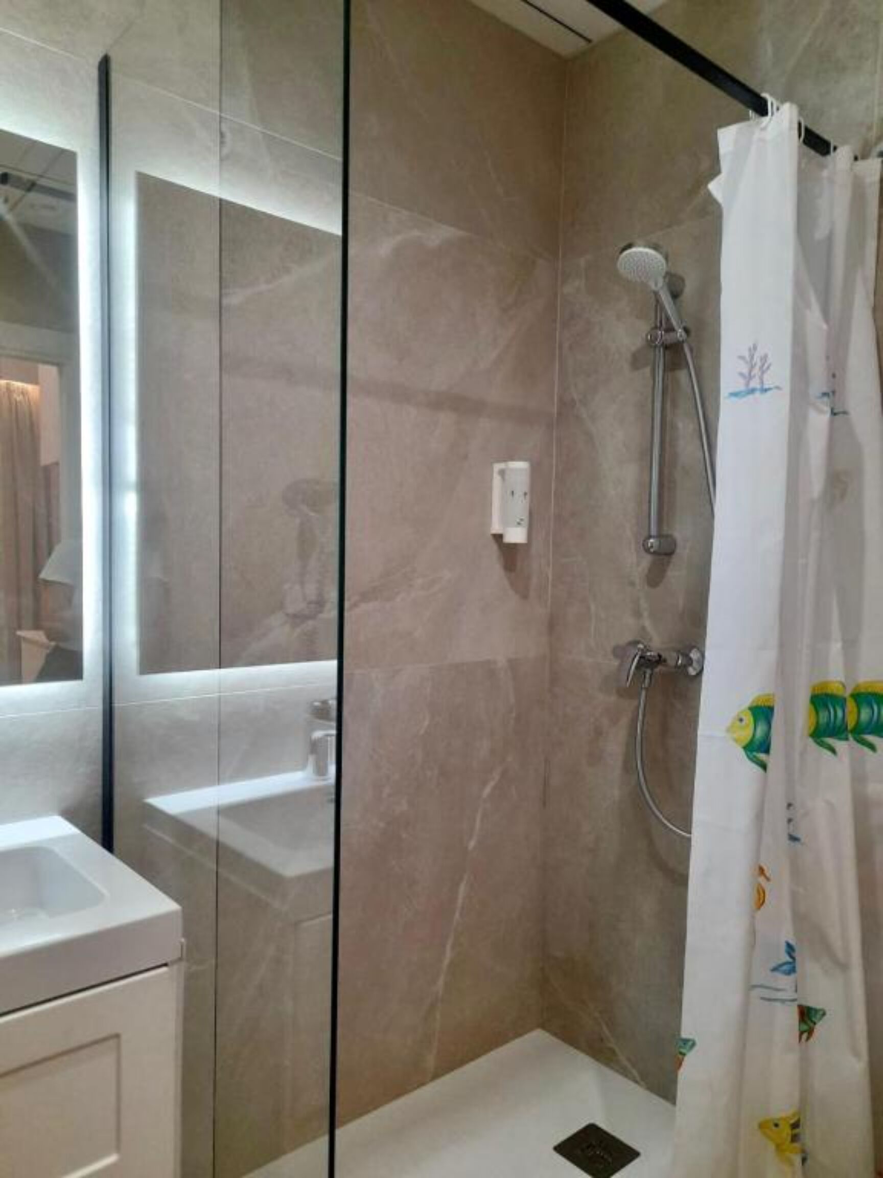 A modern bathroom with a glass shower enclosure, a white sink, and a marble wall.