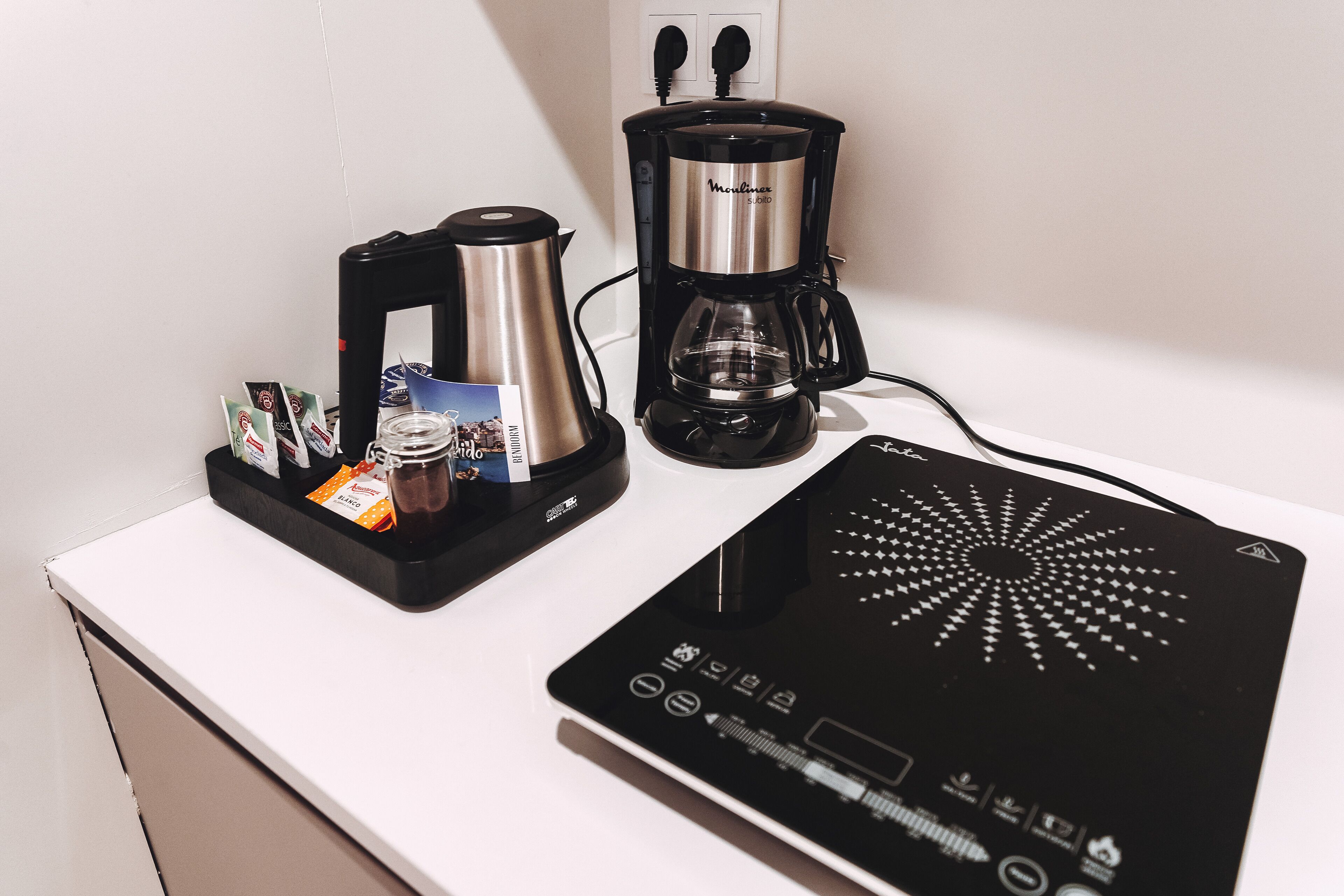 A coffee maker, a kettle, and a digital scale on a white countertop.