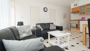 A modern living room with a black leather sofa, a white coffee table, and a kitchen area with a stove and cabinets. - Apartment in a Quiet, Rural Area, not far From the Centre (Callantsoog)