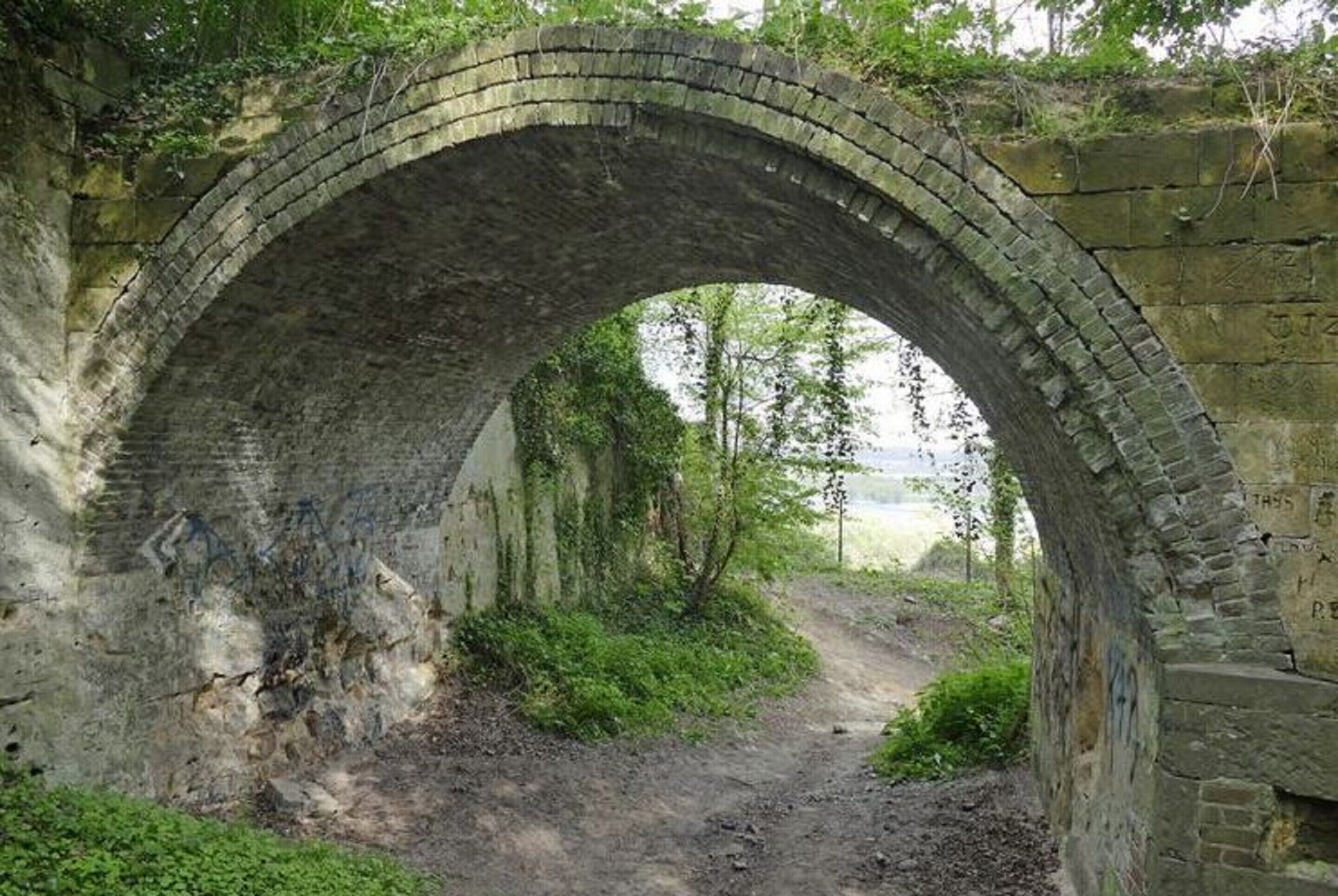 Un vieux pont de pierre avec un chemin de terre en dessous.