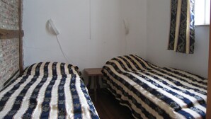 Ein Zimmer mit zwei Betten, einem kleinen Tisch, einer Steckdose und einem gerahmten Bild.