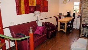Ein gemütliches Wohnzimmer mit einem roten Sofa, einem Holzespeisetisch und einer Küchenzeile mit Mikrowelle und Kaffeemaschine.
