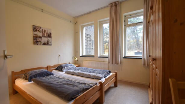 A bedroom with two wooden beds, a radiator, and a window with curtains. - Timeless Charm and Cozy Stay (Bergen aan Zee)