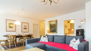 Ein Wohnzimmer mit grauem Sofa, einem kleinen Tisch und einem Essbereich mit Holzsesseln und einem Tisch.