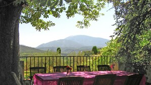 A table set outdoors with chairs, a view of hills, and a tree in the foreground. - Holiday Home Near Mont Ventoux Pool (Vaison-la-Romaine)