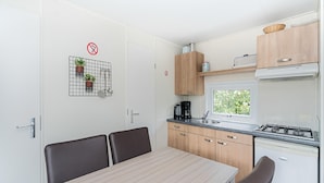 A compact kitchen with a dining table, chairs, a coffee maker, and a stove. - Chalet in Holiday Park With Private Terrace (Baarle-Nassau)
