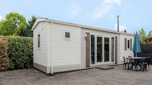 A mobile home with a patio area, a table with chairs, and a blue umbrella. - Chalet in Holiday Park With Private Terrace (Baarle-Nassau)