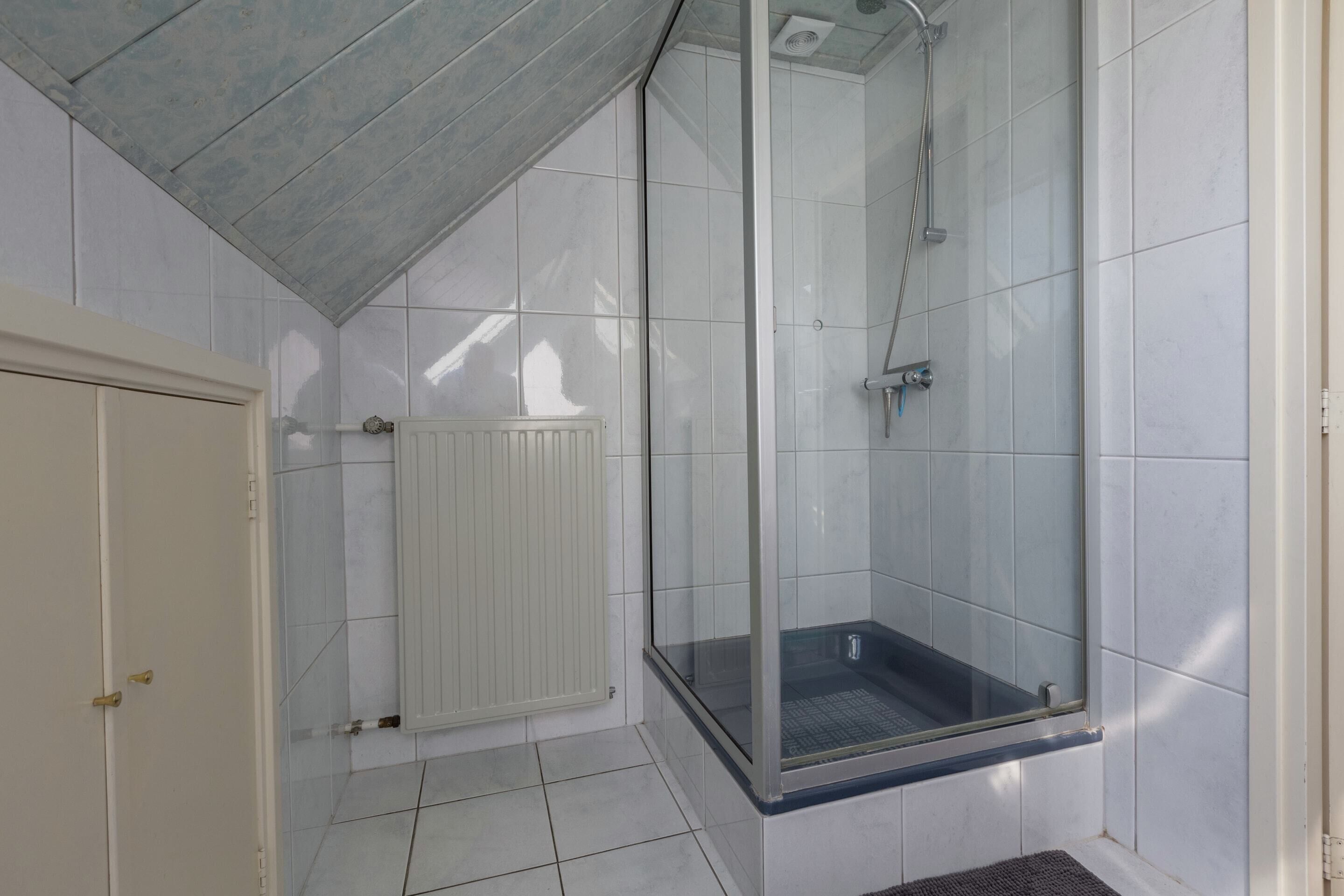 A shower with a glass door, a white radiator, and a tiled floor.