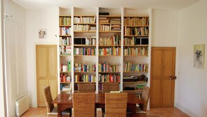 A room with a dining table, four wicker chairs, a bookshelf filled with books, and a wooden door. - Mansion in Provence With Pool & Near Town (Valreas)