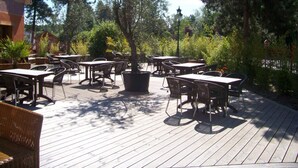 Een terras buiten met tafels en stoelen, omringd door bomen en een gebouw.